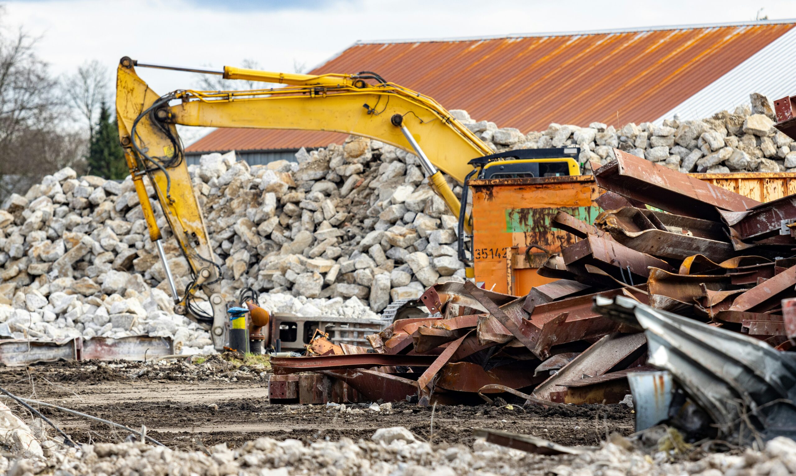 Excavator beside piles of concrete and scrap at a waste yard