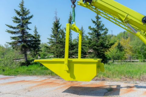 Lime crane skip hanging from a boom among trees