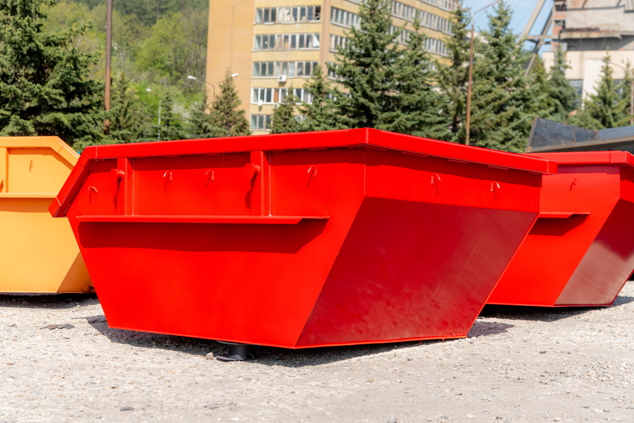 Red and orange waste skip containers in a yard